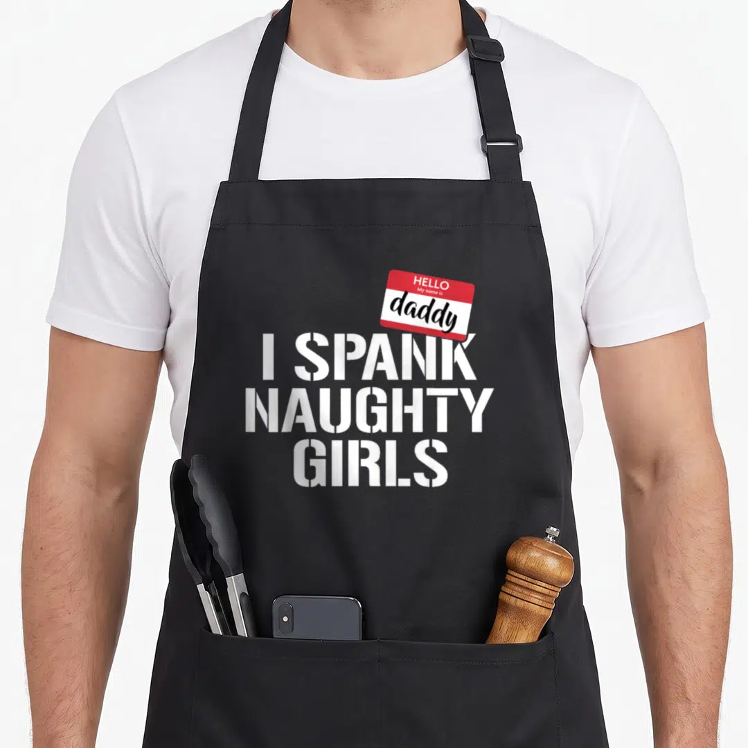 Spank daddy apron - Hello My name is daddy name tag and I SPANK NAUGHTY GIRLS stencil text on black — shown on a black cotton canvas apron against a white background