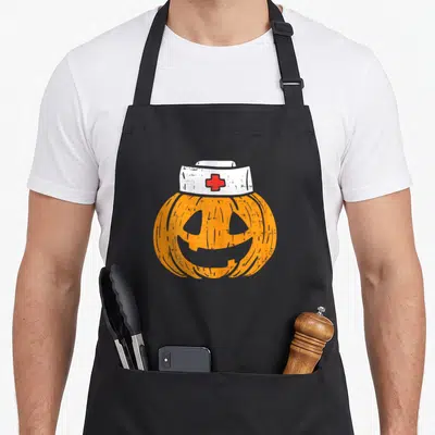 Pumpkin halloween nurse apron - Orange cartoon pumpkin wearing white nurse hat with red cross emblem — shown on a black cotton canvas apron against a white background