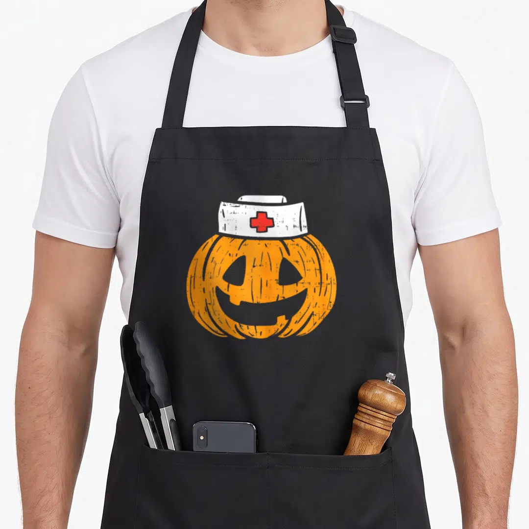 Pumpkin halloween nurse apron - Orange cartoon pumpkin wearing white nurse hat with red cross emblem — shown on a black cotton canvas apron against a white background