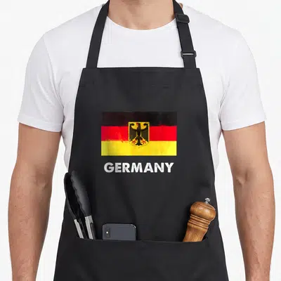 Germany flag german apron - distressed Germany flag with black red yellow stripes and white GERMANY text — shown on a black cotton canvas apron against a white background
