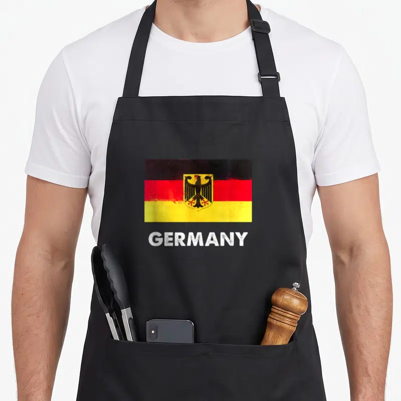Germany flag german apron - distressed Germany flag with black red yellow stripes and white GERMANY text — shown on a black cotton canvas apron against a white background