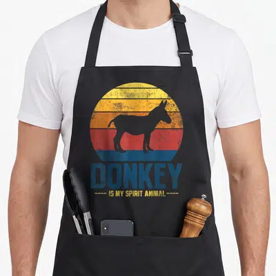 Donkey farmer apron - Grey donkey silhouette over striped retro sun with blue and yellow text — shown on a black cotton canvas apron against a white background
