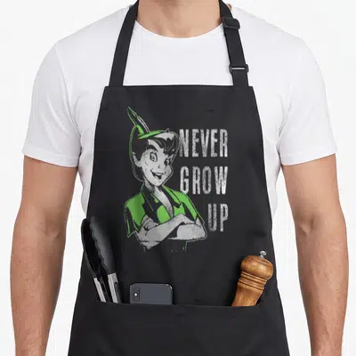 Grow bell apron - Peter Pan crossed arms green shirt distressed NEVER GROW UP text stacked vertically — shown on a black cotton canvas apron against a white background