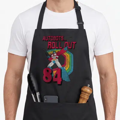 Autobot stripe apron - Optimus Prime holding gun before rainbow arc with 84 text in retro style — shown on a black cotton canvas apron against a white background