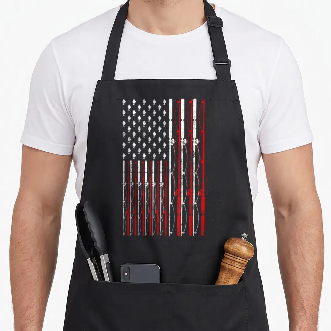 Cute fishing american flag apron - Red white fishing rod flag with fish stars distressed graphic — shown on a black cotton canvas apron against a white background