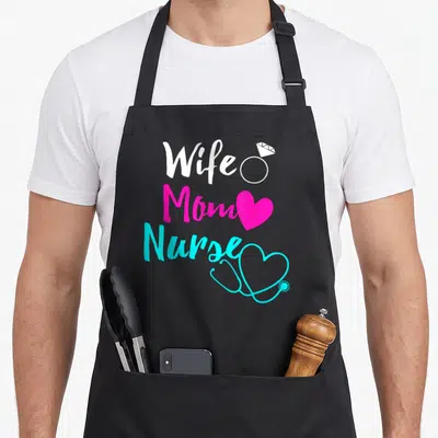 Wife nurse apron - Stacked text Wife Mom Nurse with ring heart and stethoscope icons in white pink cyan — shown on a black cotton canvas apron against a white background