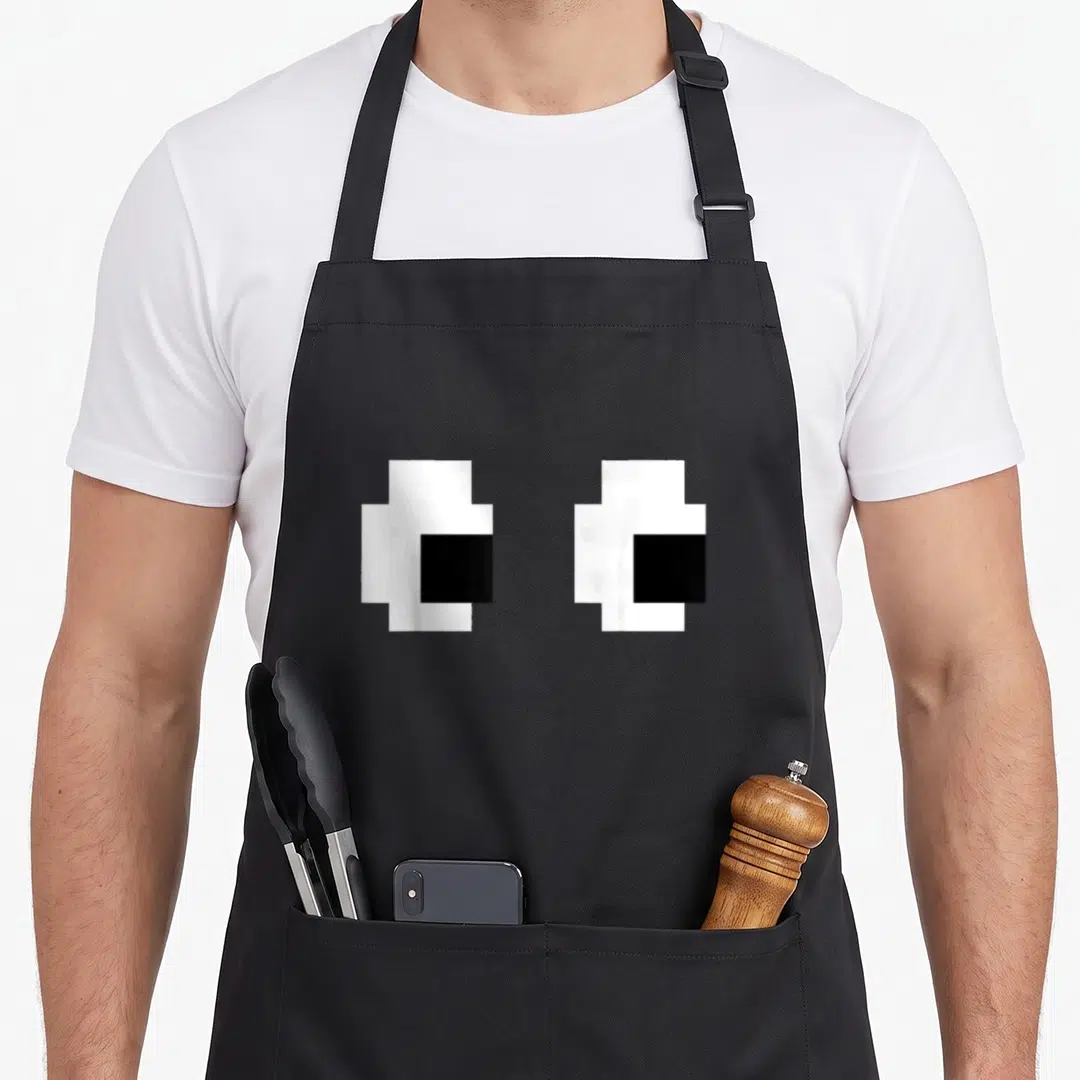 Arcade halloween apron - Two white pixelated eyes with black pupils on gray background — shown on a black cotton canvas apron against a white background