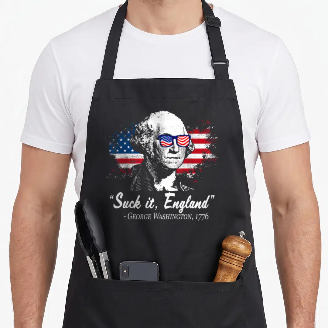Suck england 4th of july apron - George Washington portrait in sunglasses with distressed flag and Suck it England quote — shown on a black cotton canvas apron against a white background