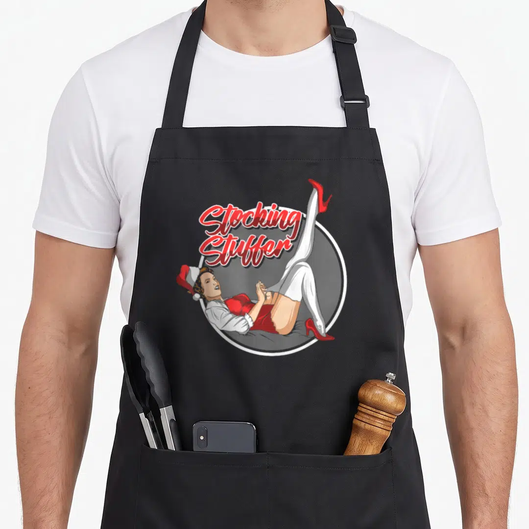 Stuffer womens christmas aprons - Pin-up girl in red dress with Stocking Stuffer text inside white circle border — shown on a black cotton canvas apron against a white background