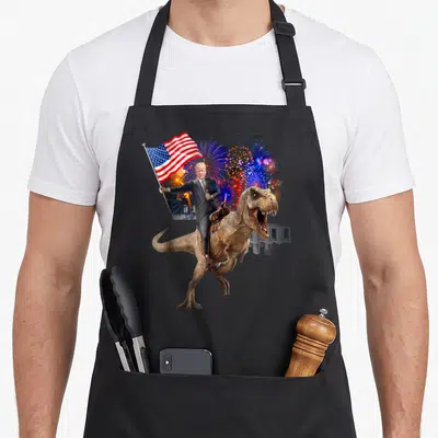 Trump dinosaur apron - Donald Trump riding a T-Rex holding a USA flag with fireworks and White House in red white blue — shown on a black cotton canvas apron against a white background