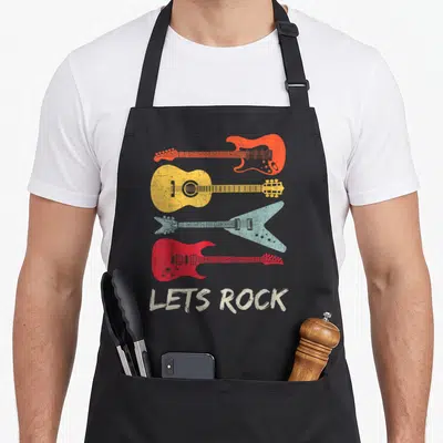 Roll rock girl apron - Four stacked guitars in orange yellow blue and red above distressed white LETS ROCK text — shown on a black cotton canvas apron against a white background