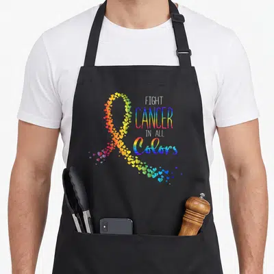 Suck cancer man apron - Rainbow ribbon made of hearts next to stacked text FIGHT CANCER IN ALL COLORS — shown on a black cotton canvas apron against a white background
