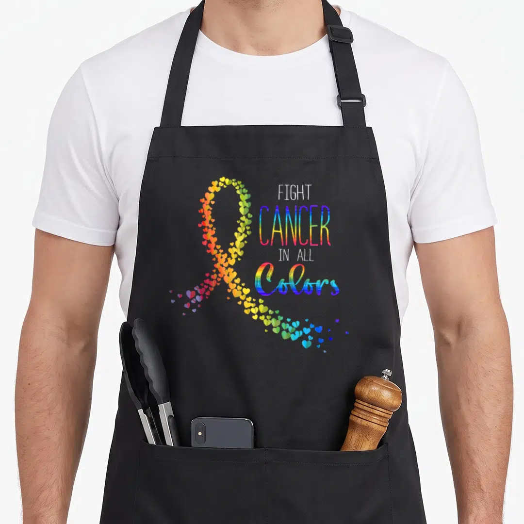 Suck cancer man apron - Rainbow ribbon made of hearts next to stacked text FIGHT CANCER IN ALL COLORS — shown on a black cotton canvas apron against a white background