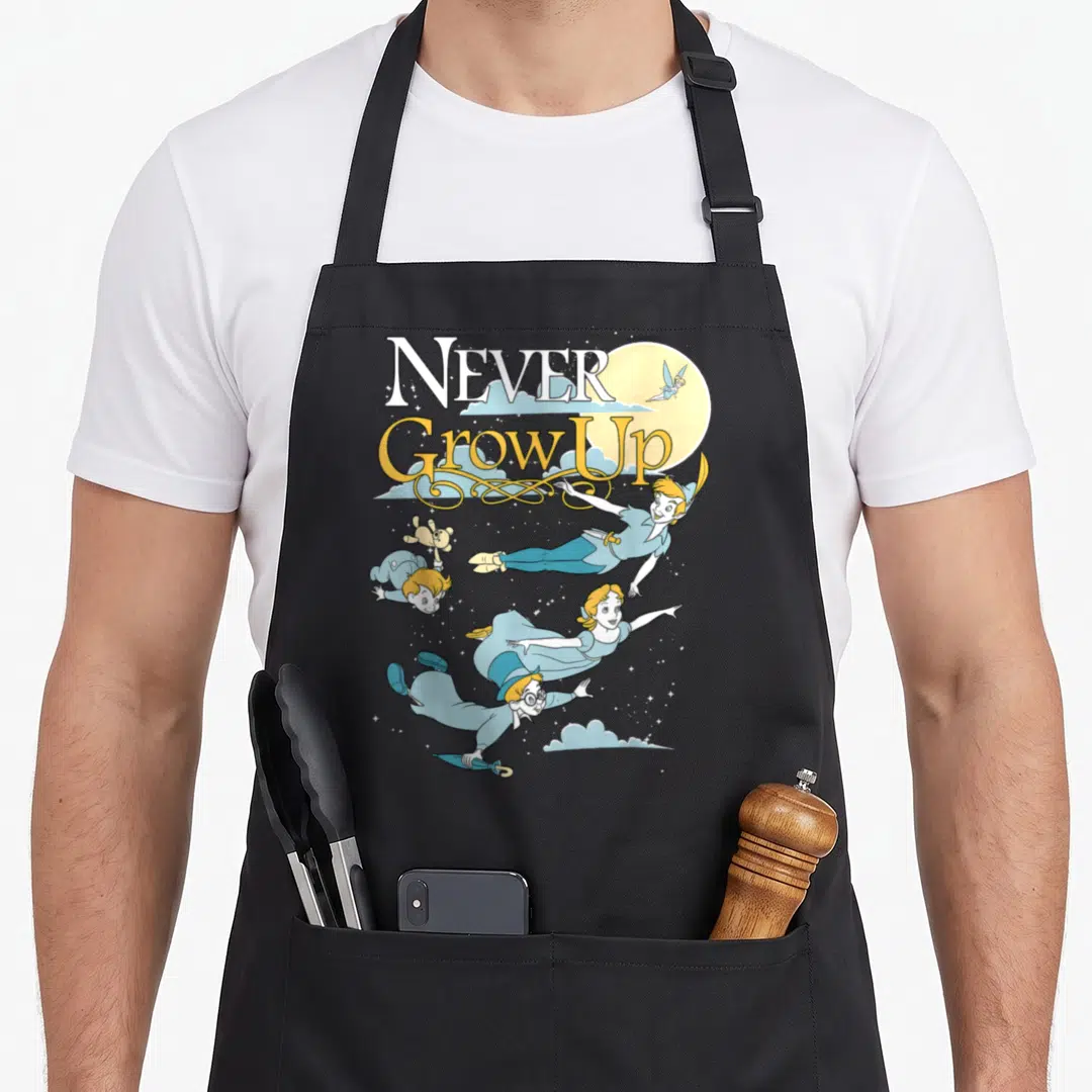 Peter night apron - NEVER Grow Up text with Peter Pan group flying near moon and Tinker Bell in blue and yellow — shown on a black cotton canvas apron against a white background