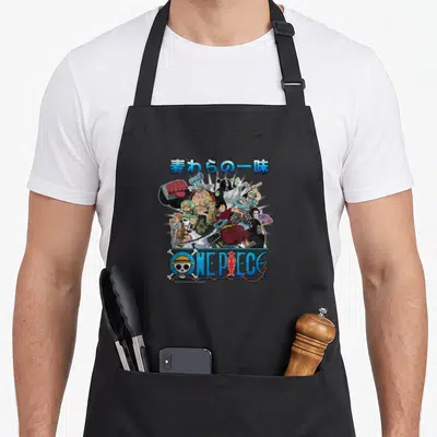 Straw anime apron - Japanese text, Straw Hat Pirates cluster, ONE PIECE skull logo on black apron — shown on a black cotton canvas apron against a white background