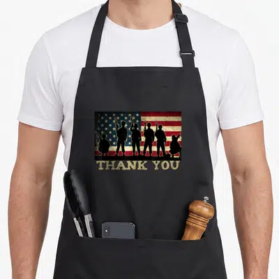 Thank patriotic apron - Six soldier silhouettes on distressed flag with THANK YOU text below — shown on a black cotton canvas apron against a white background