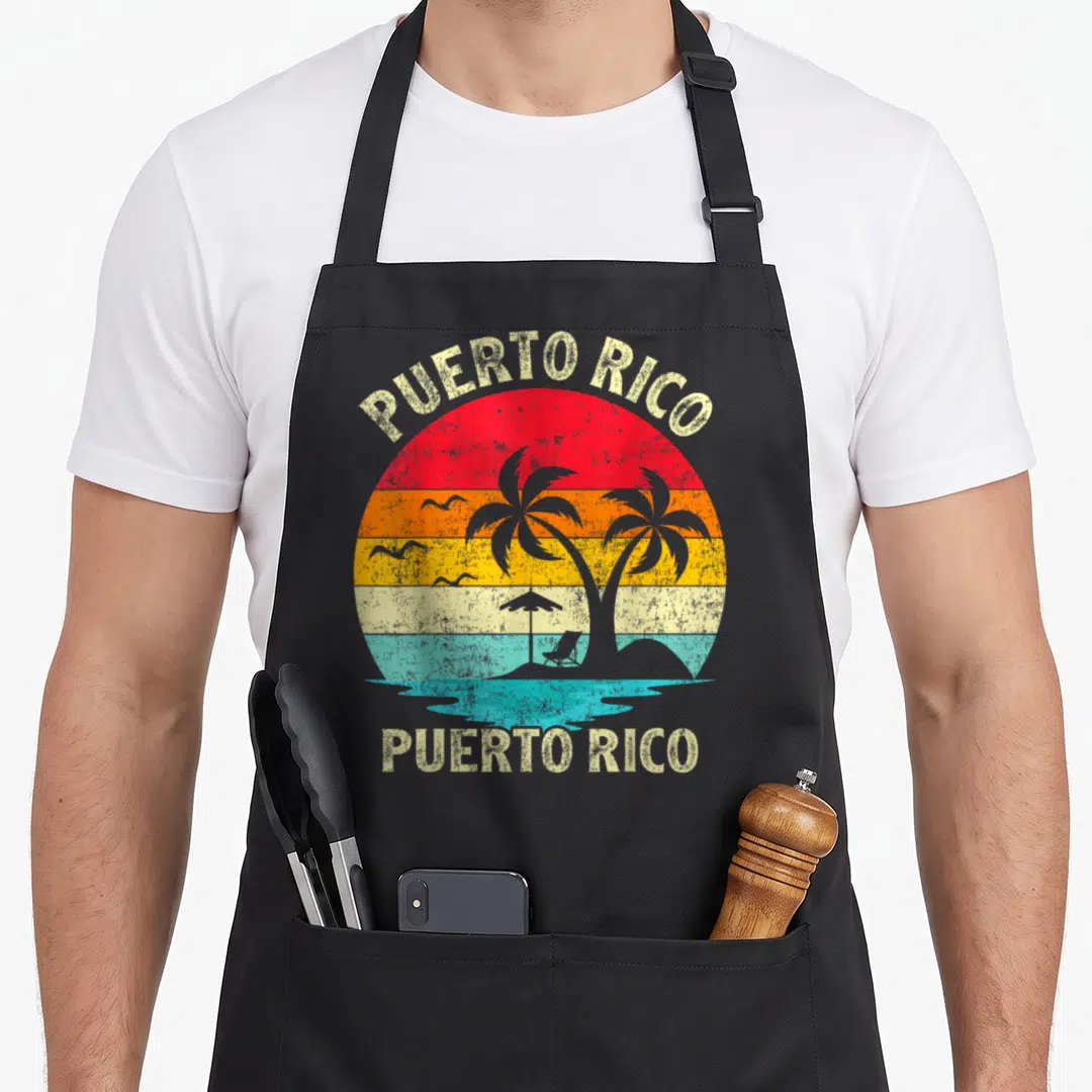 Puerto family aprons - Retro circular sunset with palm trees, beach chair, umbrella, birds, and text PUERTO RICO above — shown on a black cotton canvas apron against a white background