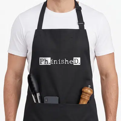 Graduation student aprons - White Ph.inisheD text on black background — shown on a black cotton canvas apron against a white background