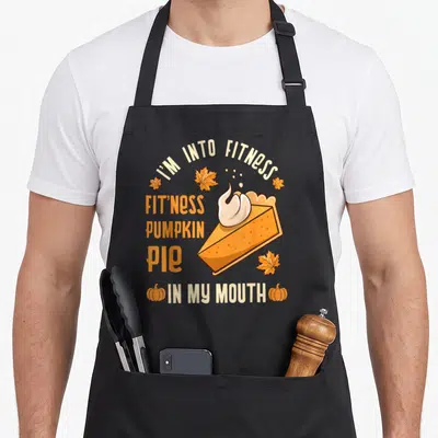 Cool turkey thanksgiving day aprons - Cartoon pumpkin pie slice with whipped cream and fitness pun text surrounded — shown on a black cotton canvas apron against a white background