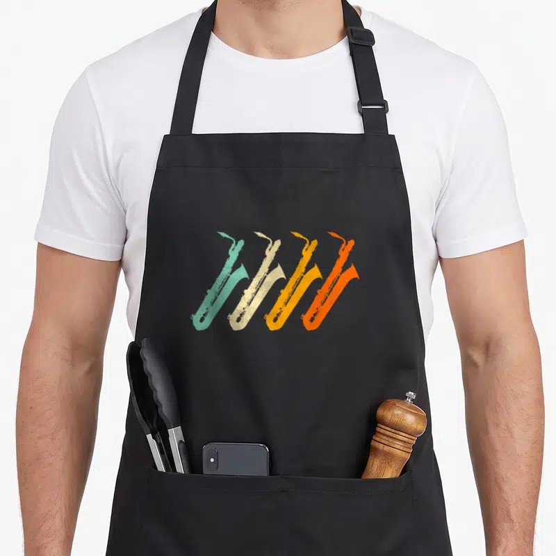 Baritone saxophonist apron - Four retro saxophones in teal, beige, yellow, and orange arranged diagonally — shown on a black cotton canvas apron against a white background