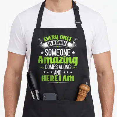 Amazing come and get it apron - Stacked lime green and white text with banner and stars saying Everyone Once In A While — shown on a black cotton canvas apron against a white background