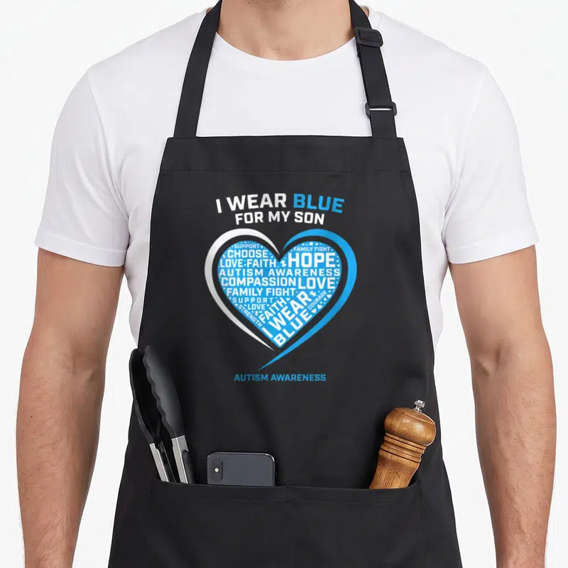 Awareness dad and son aprons - Blue and white heart filled with Autism Awareness supportive words and I WEAR BLUE — shown on a black cotton canvas apron against a white background