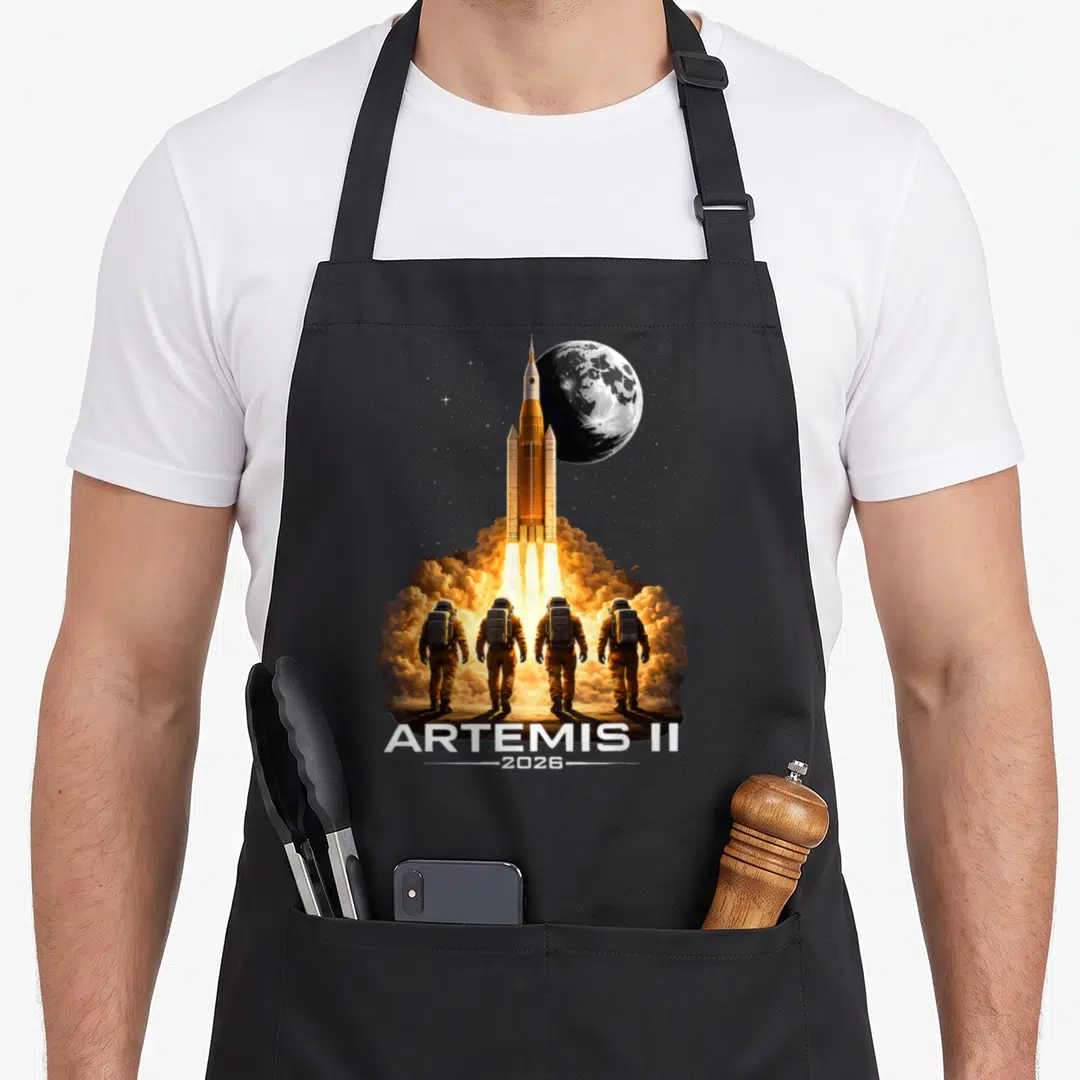 Artemis boy astronaut apron - Orange rocket launching vertically with four astronauts and ARTEMIS II 2026 text — shown on a black cotton canvas apron against a white background