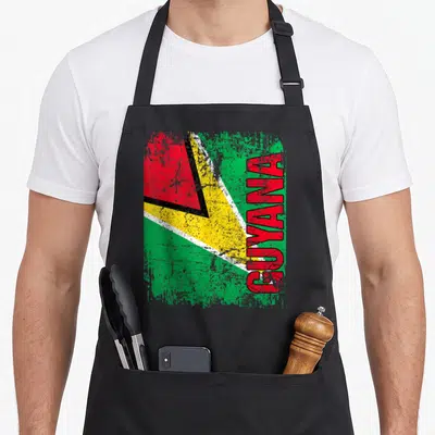 Guyana distressed apron - Vertical GUYANA text over a distressed green yellow and red flag design — shown on a black cotton canvas apron against a white background