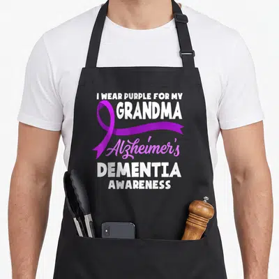 Alzheimer grandma apron - Purple ribbon overlaps vertical white text reading I WEAR PURPLE FOR MY GRANDMA Alzheimer's — shown on a black cotton canvas apron against a white background