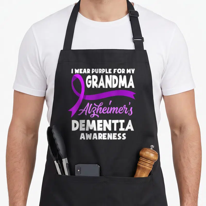 Alzheimer grandma apron - Purple ribbon overlaps vertical white text reading I WEAR PURPLE FOR MY GRANDMA Alzheimer's — shown on a black cotton canvas apron against a white background