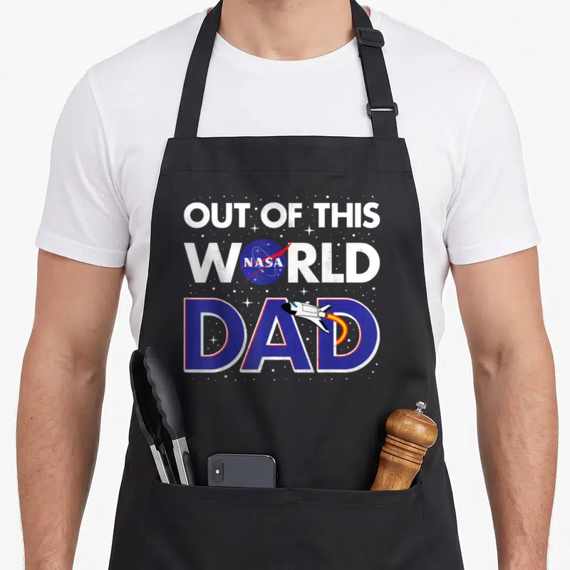 Father nasa apron - Out of This World NASA Dad text with blue planet logo and flying space shuttle — shown on a black cotton canvas apron against a white background