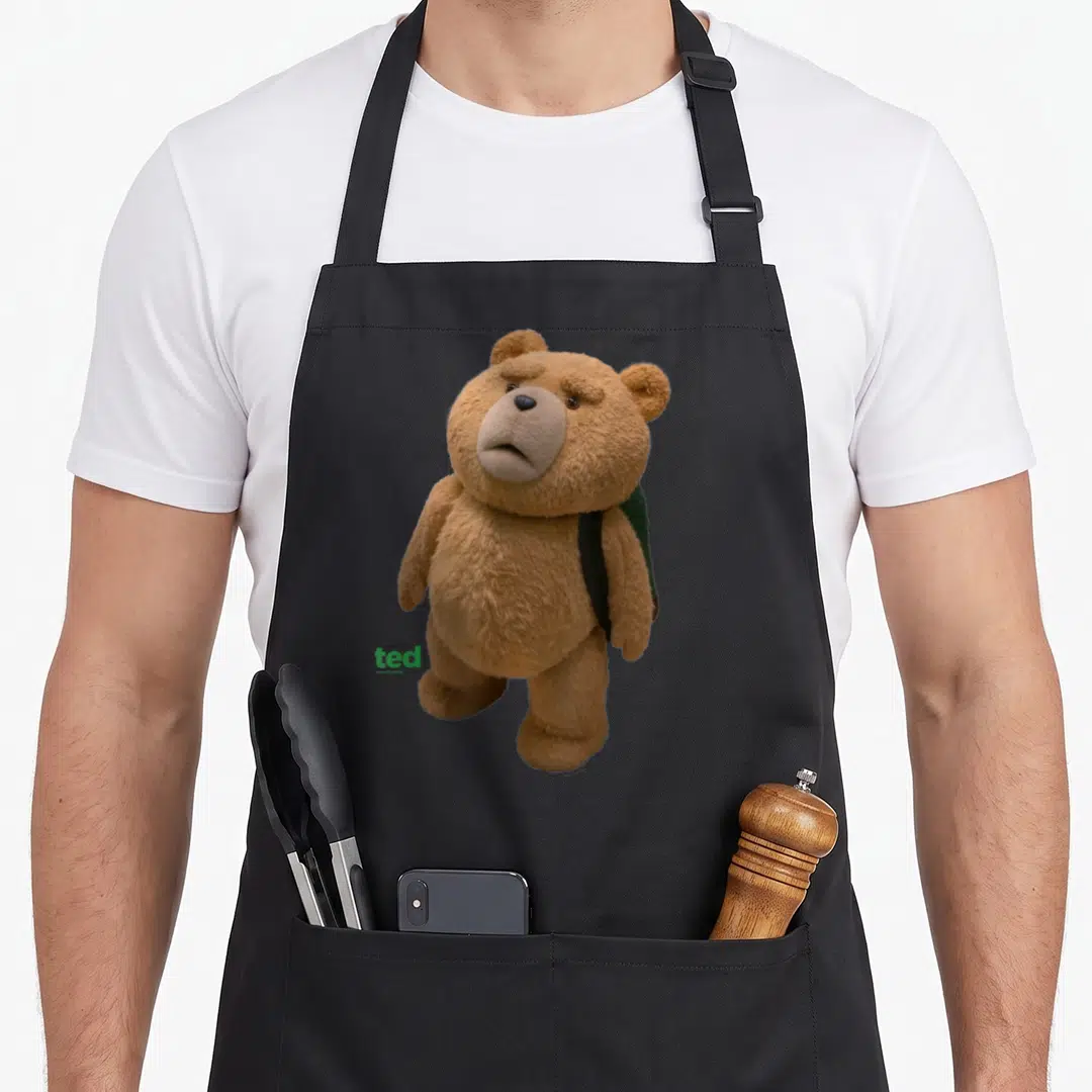 Ted teddy bear apron - Brown teddy bear wearing dark green backpack with green ted logo text — shown on a black cotton canvas apron against a white background