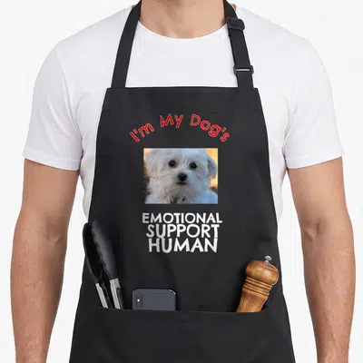 Emotional dog apron - Red script text above white dog photo and stacked white bold words — shown on a black cotton canvas apron against a white background
