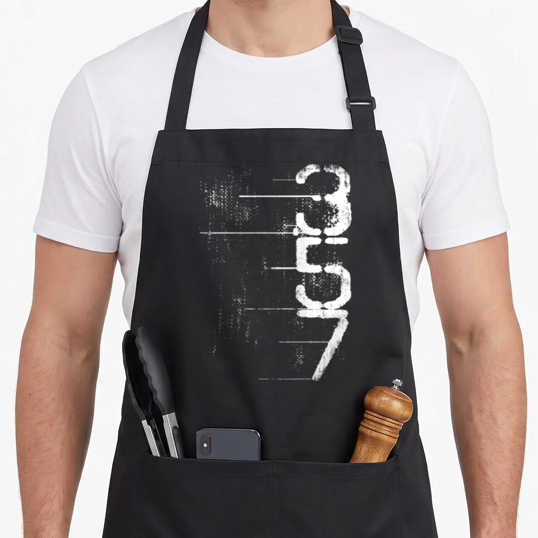 Ammo shooting apron - White distressed 357 numbers stacked vertically with horizontal streaks extending left — shown on a black cotton canvas apron against a white background