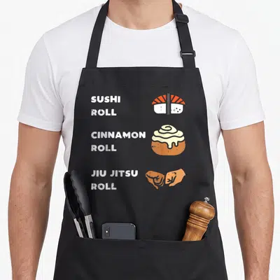 Cinnamon sushi apron - White text reading Sushi Cinnamon Jiu Jitsu Roll next to matching sushi, pastry, and grappling — shown on a black cotton canvas apron against a white background