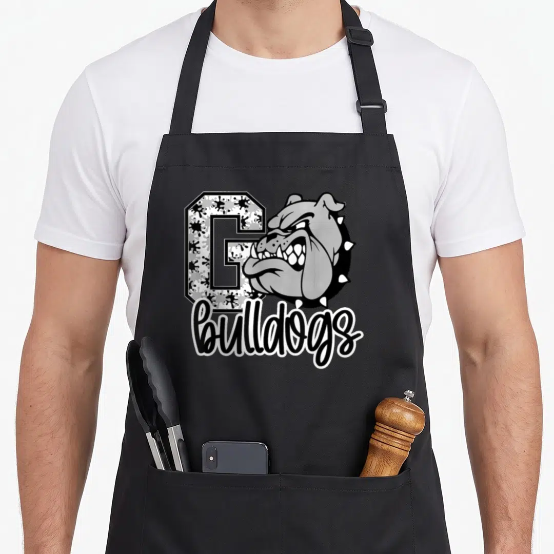 Football dog apron - Cartoon bulldog head overlapping letter G with bulldogs script text in grey and black — shown on a black cotton canvas apron against a white background