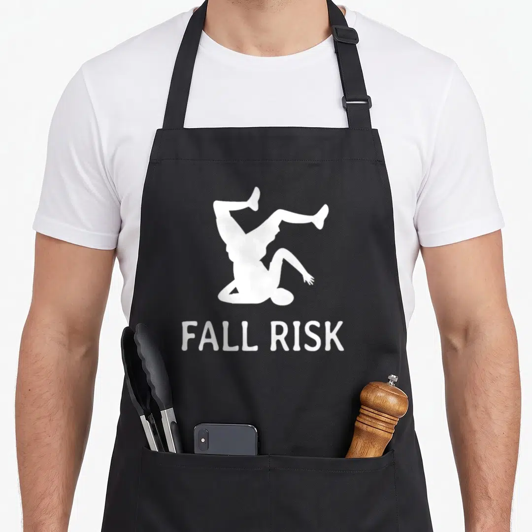 Cute risk fall apron - White silhouette of person falling above FALL RISK text in minimalist style — shown on a black cotton canvas apron against a white background