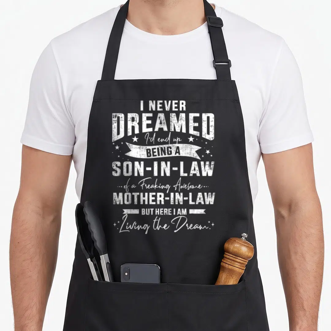 Dreamed law mother son aprons - White distressed text I Never Dreamed Being A Son-In-Law with stars and ribbons — shown on a black cotton canvas apron against a white background