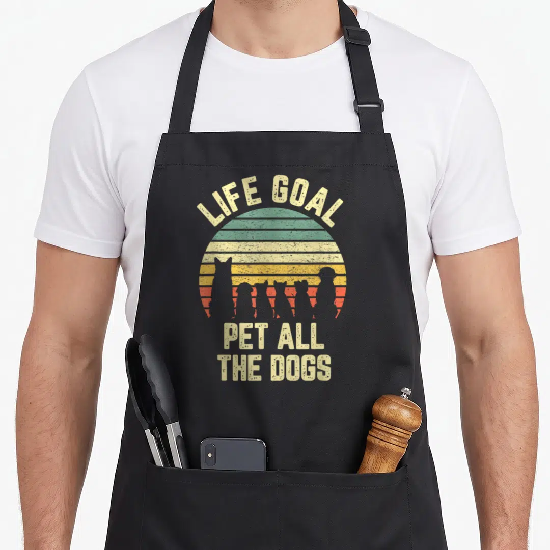 Goal funny dog apron - Retro sun with dog silhouettes and text life goal pet all the dogs — shown on a black cotton canvas apron against a white background