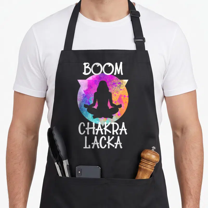 Boom grill instructor apron - White Boom Chakra Lacka text surrounding grey meditating silhouette in multicolored — shown on a black cotton canvas apron against a white background