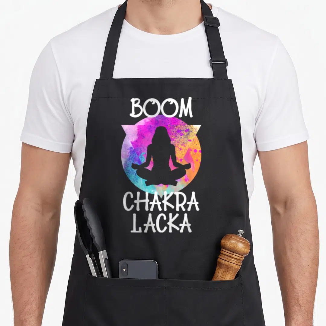 Boom grill instructor apron - White Boom Chakra Lacka text surrounding grey meditating silhouette in multicolored — shown on a black cotton canvas apron against a white background