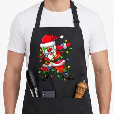 Dabbing santa apron - Cartoon Santa in red suit tangled in green wire Christmas lights doing a dab pose — shown on a black cotton canvas apron against a white background