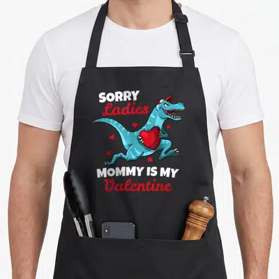 Sorry valentine's day apron - Dinosaur holding heart with text Sorry Ladies Mommy Is My Valentine — shown on a black cotton canvas apron against a white background