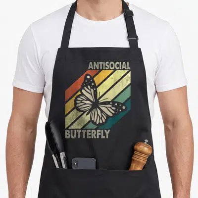 Vintage antisocial butterfly apron - Centered grey butterfly over red orange yellow green and blue diagonal stripes — shown on a black cotton canvas apron against a white background