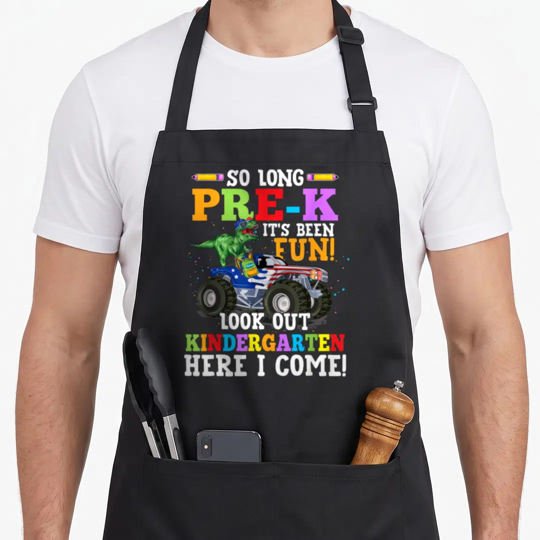 Pre kindergarten boys apron - Green dinosaur in sunglasses on monster truck with colorful Pre-K graduation text — shown on a black cotton canvas apron against a white background