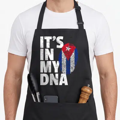 Cuba pride apron - Distressed IT'S IN MY DNA text next to red white and blue fingerprint shaped like Cuban flag — shown on a black cotton canvas apron against a white background