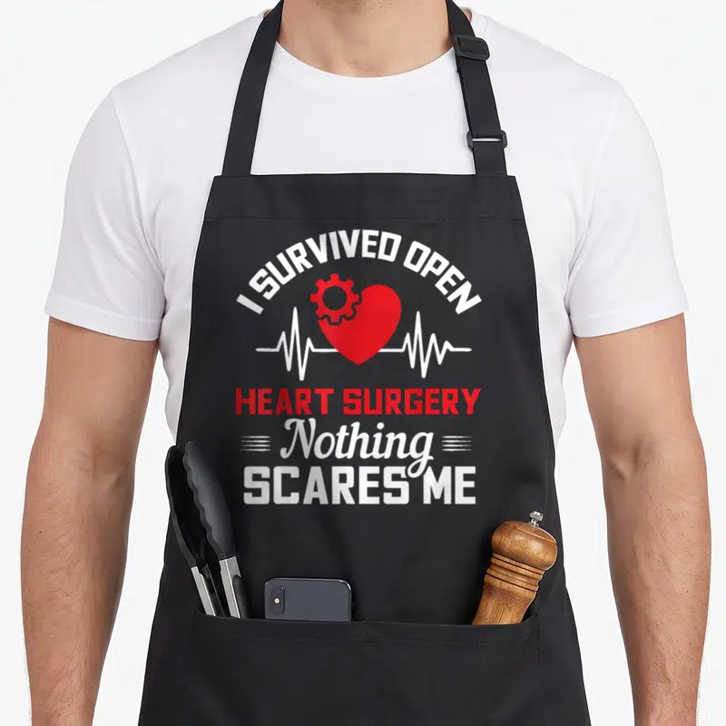 Survived open apron - Red gear-heart over white EKG line with stacked I SURVIVED OPEN HEART SURGERY NOTHING SCARES ME — shown on a black cotton canvas apron against a white background