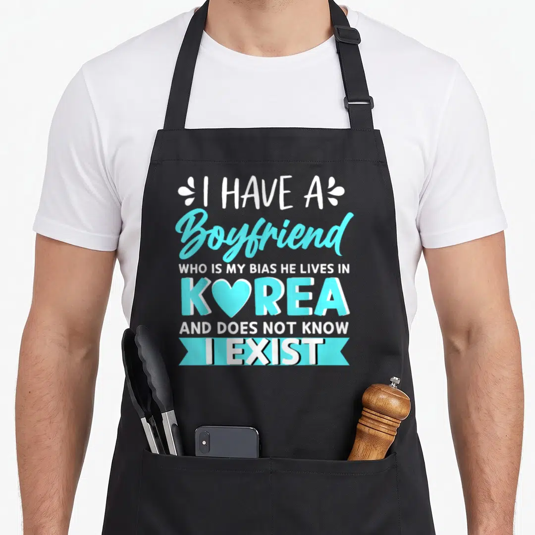 Boyfriend bias korean apron - White and cyan typography saying I Have A Boyfriend Who Is My Bias He Lives In Korea — shown on a black cotton canvas apron against a white background