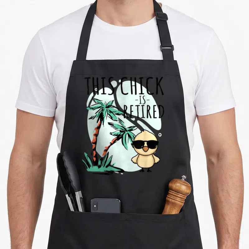 Chick retired retirement apron - Cartoon chick in sunglasses stands by two palm trees under retired text — shown on a black cotton canvas apron against a white background