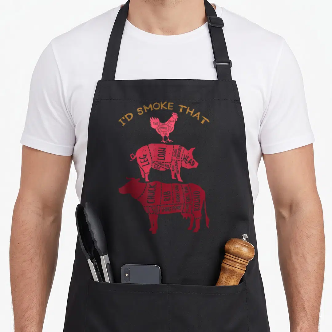 Funny smoke barbecue apron - I'D SMOKE THAT text over red and orange chicken pig cow butcher cut diagram — shown on a black cotton canvas apron against a white background
